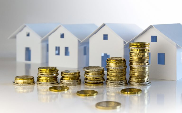 Plusieurs maisons miniatures devant lesquelles sont disposées des pièces d'euro empilées
